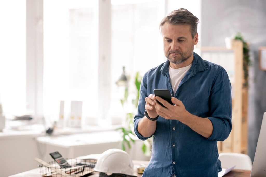 Serious engineer in casualwear scrolling through contacts in his smartphone